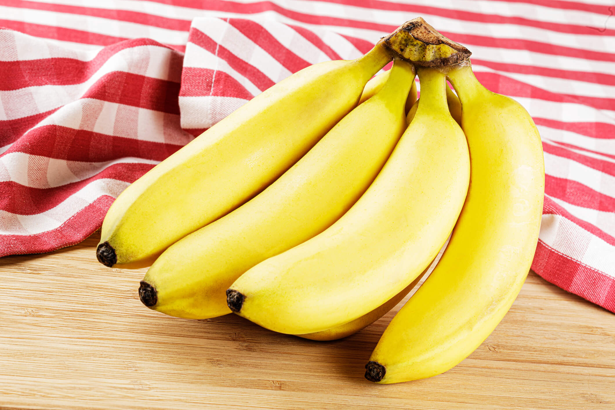 A bunch of bananas on a wooden table set against a white and red cloth