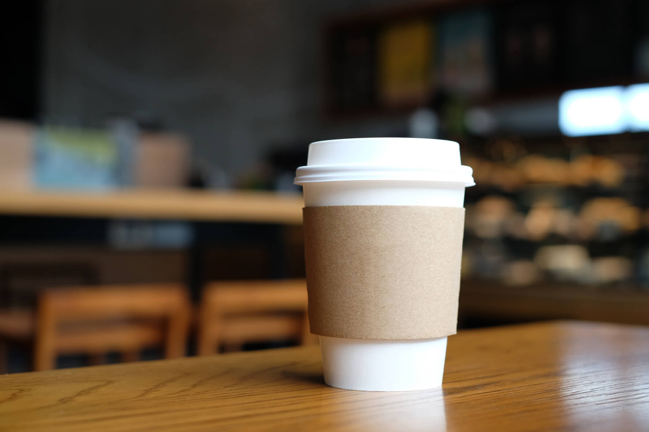 A to-go coffee cup on a wooden table, with the blurred interior coffee shop as the background
