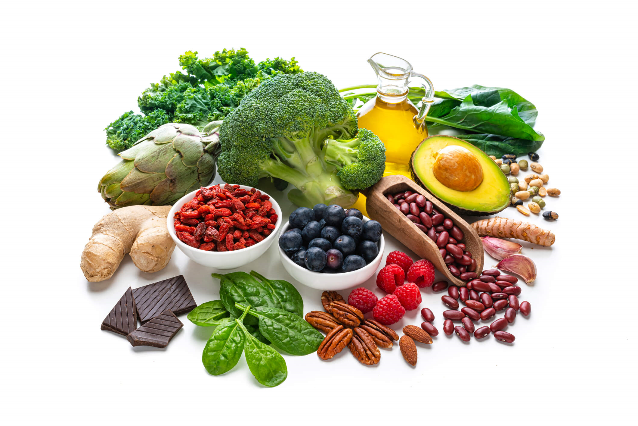 An assortment of foods that are high in antioxidants against a white background. The foods include broccoli, kidney bean, blueberries, raspberries, spinach, ginger, dark chocolate, kale, almonds, and artichoke