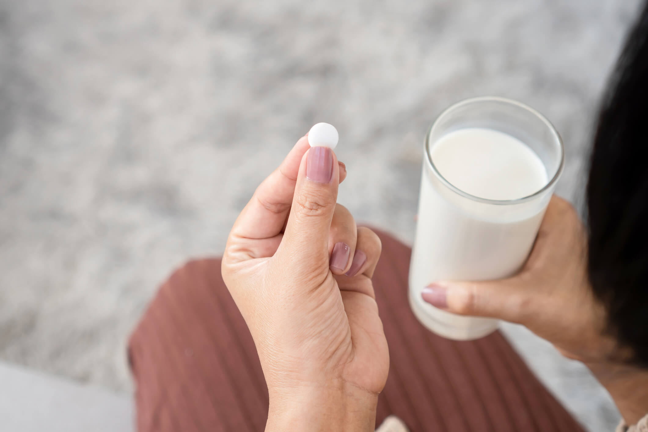 This is a photo from the perspective of a woman looking down at her hands. In one hand there is a pill, and in the other is a glass of milk.