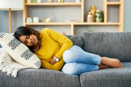 Woman on couch holding stomach due to abdominal pain.