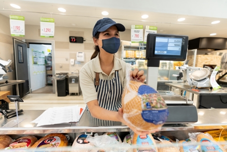 Woman working in supermarket selling a frozen turkey to a customer while wearing a protective face mask. | Advance ER