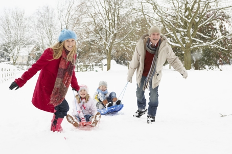 Mother And Father Pulling Children On Sledge Through Snowy Landscape