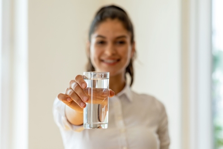 Woman smiling while holding up a water glass, encouraging proper hydrated practices for her loved ones. | Advance ER