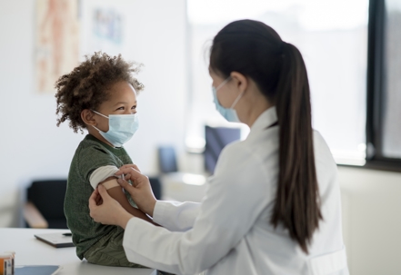 Pediatric doctor placing a Band-Aid on a little boy’s arm after administering a vaccine in preparation of the new school year. He is smiling as she tells him he did a great job before leaving. | Advance ER