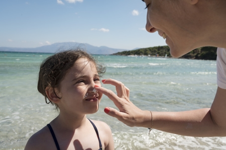 Mother applying sunscreen to her daughter's face at the beach.