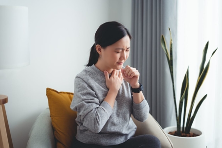 Woman with throat pain holding hand to throat.