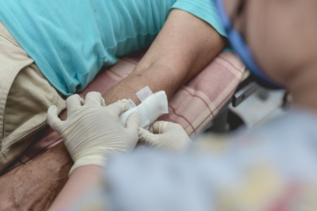 Applying medical tape to secure clean dressing to a disinfected dog bite wound on the forearm of a patient at a bite center or local clinic.