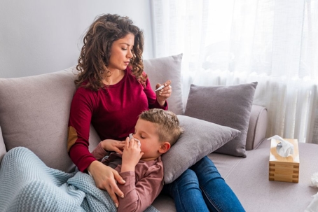 mother-sitting-with-sick-son-on-couch-checking-his-temperature