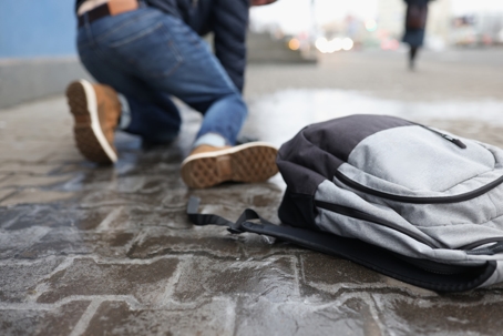 Person slipping on a wet sidewalk during rainy weather, with a backpack on the ground in the foreground, illustrating a slip and fall accident.