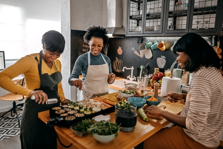 Three women cooking together in a warm kitchen preparing Thanksgiving dishes and enjoying the holiday meal prep