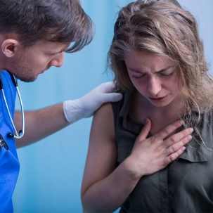Woman holding her chest as a doctor examines her